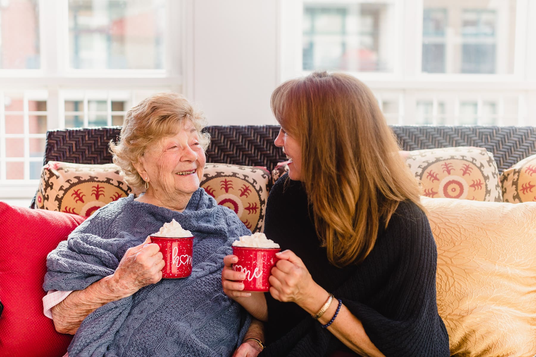 elderly woman and caregiver sitting on couch drinking coffee