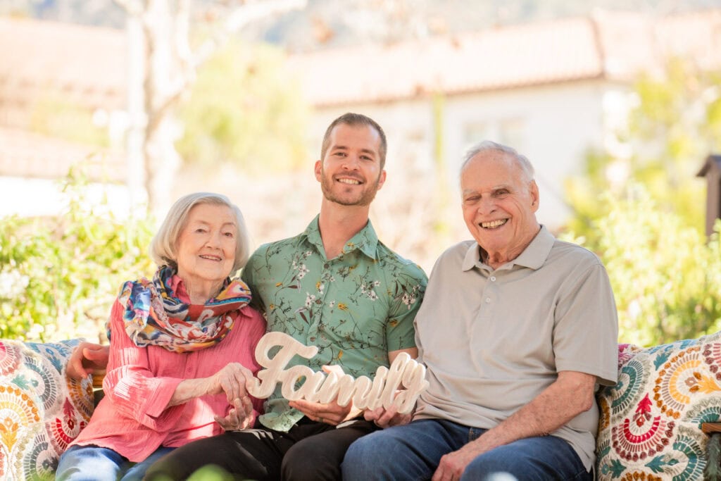 older couple sitting with young man holding sign that says family