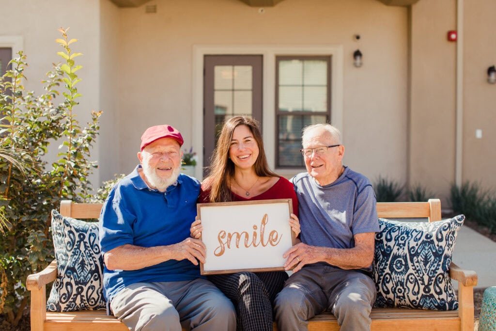 two old men sitting with young woman holding sign that says smile